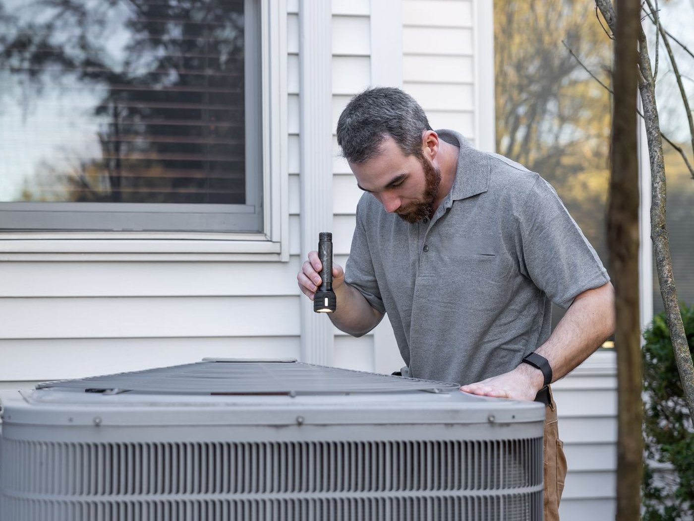 Illustrative photo: a technician checking an outdoor aircon unit